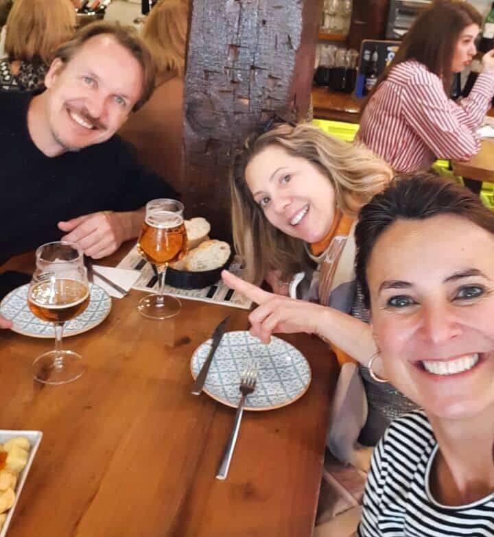 Clientes da Thais almoçando junto com ela em um dos roteiros de viagem. Eles bebem chopp e estão sorrindo.